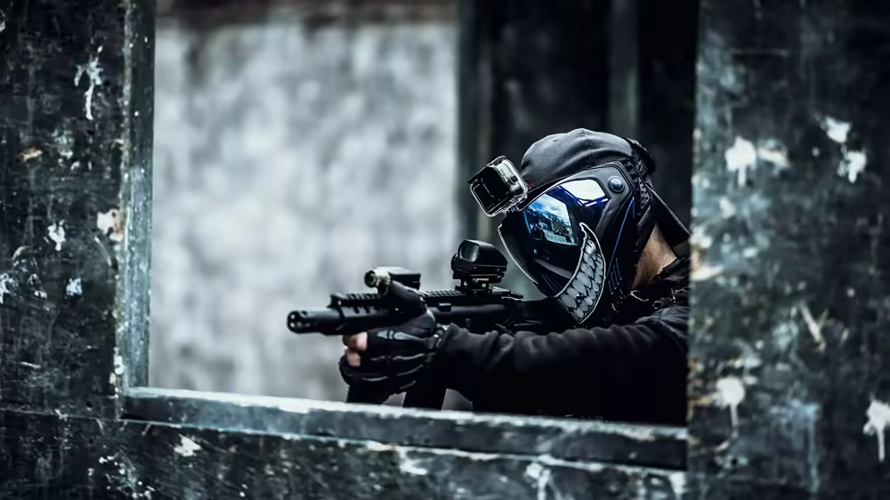 Airsoft player with tactical helmet aiming over a barricade at an opponent