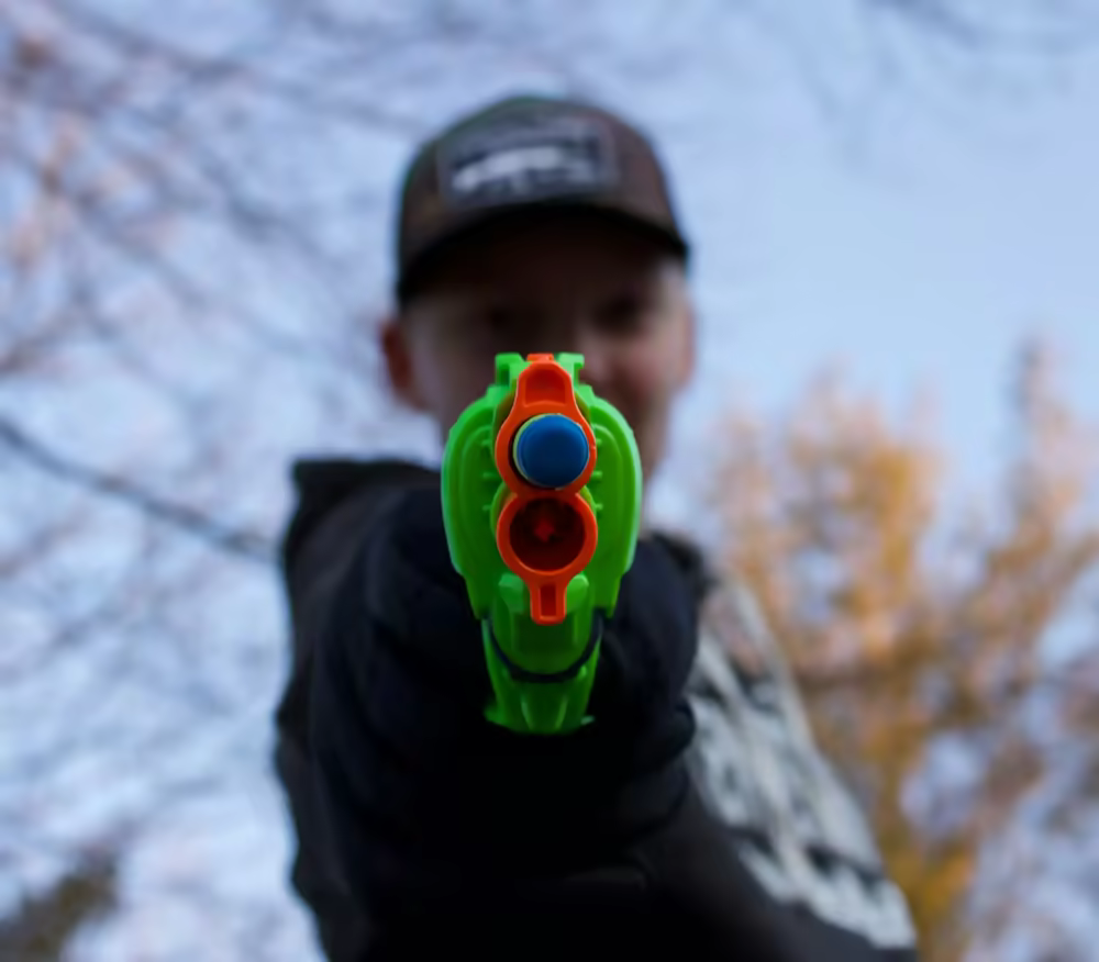 Young kid aiming a Nerf blaster at the camera with a cool and cheeky expression