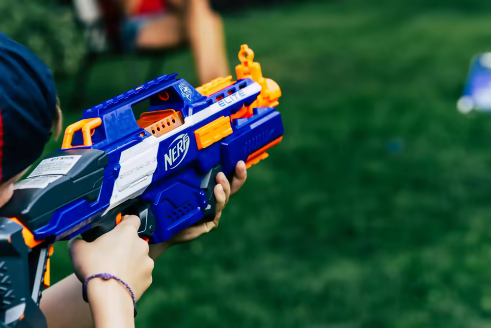 Young kid holding a Nerf blaster while aiming and firing during a battle